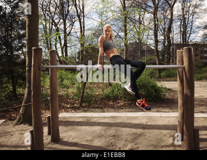 Fit young female sitting on parallel bars. Woman taking rest after triceps dips exercise at park. Stock Photo