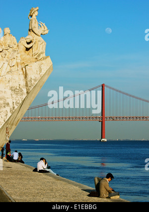 River Tagus scene with tourists, Monument of Discoveries, April 25th bridge and daytime moon, Lisbon Portugal western Europe Stock Photo