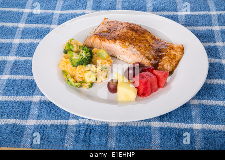 A plate of fresh, baked salmon with a broccoli, cheese and rice casserole and fresh cut fruit Stock Photo