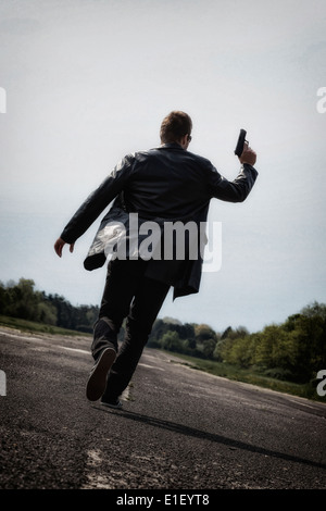 a man running on an abandoned street with a gun Stock Photo