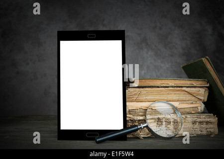 Old yellowed books and self-designed tablet-computer with blank display and a magnifying glass Stock Photo
