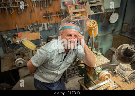The aged man leaned his elbow on the wood lathe in home workshop. Stock Photo