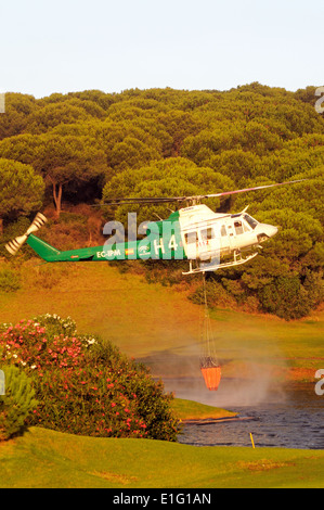 Bell 412 registration EC-IPM collecting water for fire fighting from a golf club lake, Cabopino Golf, Andalucia, Spain, Europe. Stock Photo