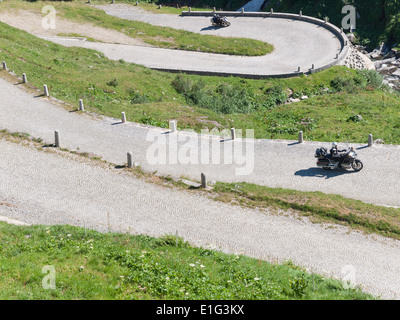 Motorbike tourists drive up the cobble stone paved road ('Tremola') on the historic mountain pass of San Gottardo, Switzerland. Stock Photo