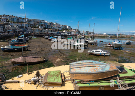 BRIXHAM HARBOUR in Devon at low tide with boats and yachts moored . Boat with dinghy on deck in foreground.Houses in background Stock Photo