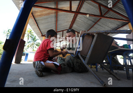U.S. Marine Corps Cpl. Paul Fuit, right, assigned to 2nd Marine Logistics Group, shows a child how to use a rasp to smooth wood Stock Photo