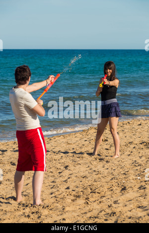Caucasian couple playing with squirt guns on beach Stock Photo - Alamy