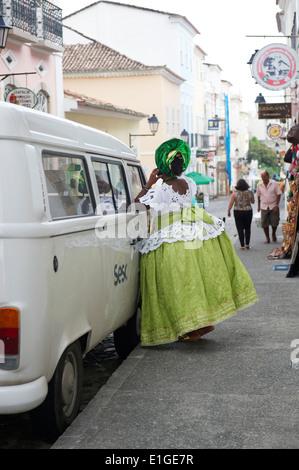 SALVADOR, BRAZIL - OCTOBER 15, 2013: Woman in traditional Baiana costume stands leaning on a Volkwagen Kombi. Stock Photo