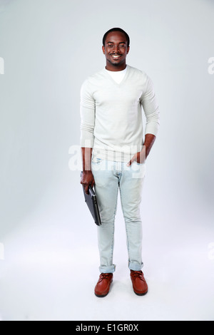 Full length portrait of african man standing with laptop on gray background Stock Photo