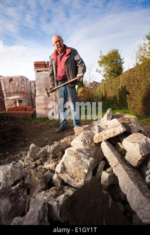 self building house, heavy manual work, middle aged man using sledgehammer to break concrete Stock Photo