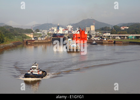 Approaching the Mira Flores lock in the Panama Canal, tug boat is in front & cargo ships are in the chambers, Panama. Stock Photo