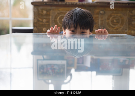 Portrait of boy peeking over dining room table Stock Photo