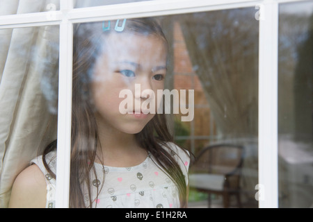 Unhappy young girl looking out from sitting room window Stock Photo