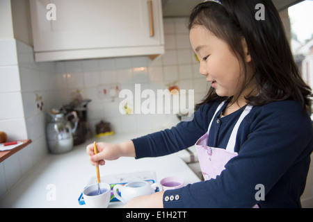 Young girl dipping paintbrush in water bowl in kitchen Stock Photo
