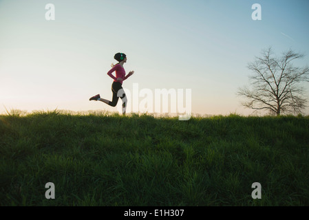 Young female runner silhouetted on hill Stock Photo