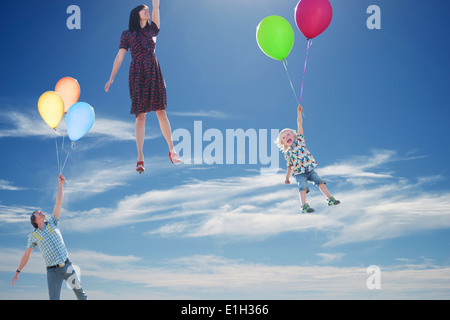 Mature couple and young son floating skyward holding onto balloons Stock Photo