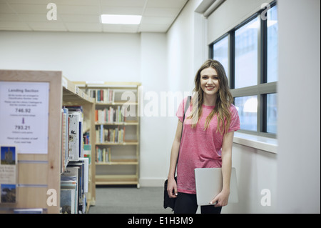 Young woman holding laptop in library
