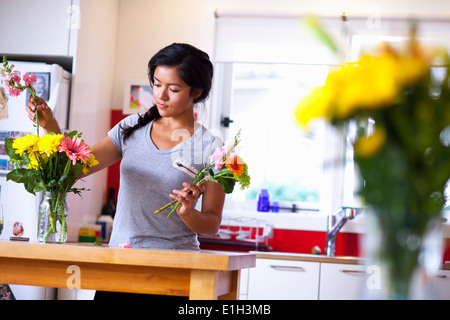 Young woman arranging flowers in kitchen Stock Photo