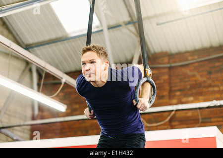 Man pulling suspended rings in gym Stock Photo