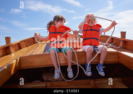 Two children sitting in boat, holding rope Stock Photo