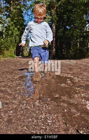 Young boy splashing in muddy puddle Stock Photo