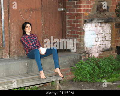 Portrait of smiling young woman on doorway step holding crockery Stock Photo