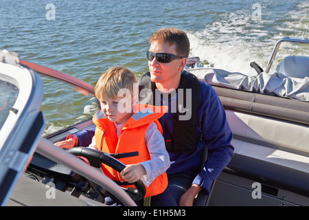 Young boy sitting on fathers lap steering motor boat Stock Photo