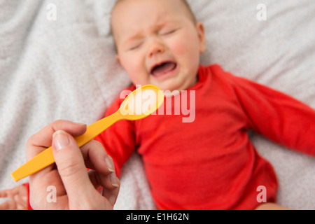 Mothers hand holding spoon to feed crying baby daughter
