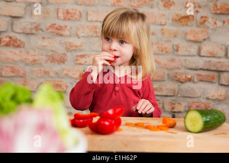 Two year old girl in kitchen eating raw vegetables Stock Photo