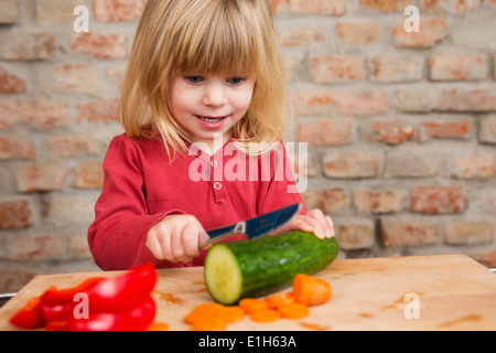 Two year old girl in kitchen learning to slice vegetables Stock Photo
