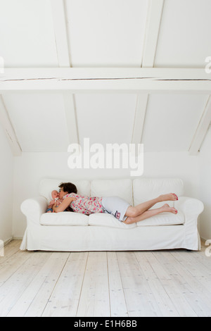 Mid adult mother lying on sofa and kissing baby daughter Stock Photo