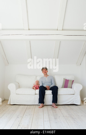 Portrait of mature father sitting next to baby daughter on sofa Stock Photo