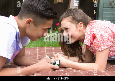 Teenage couple with smartphones lying on blanket in garden Stock Photo