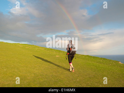 Young female hiker, hiking up hill toward rainbow Stock Photo