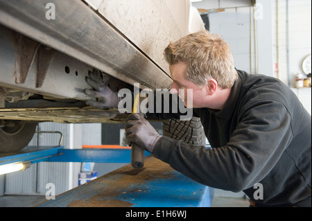 A mechanic is checking the chassis number from a lifted car on a bridge in a garage. Stock Photo