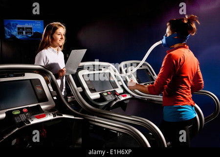Trainer monitoring mid adult woman with face mask on gym treadmill in altitude centre Stock Photo