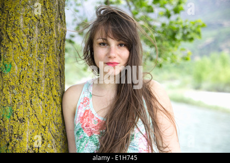 Portrait of young woman leaning against tree trunk