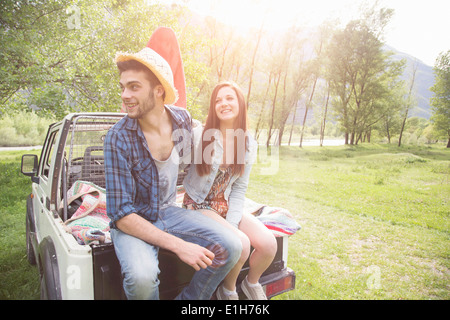 Young couple sitting on back of pick-up truck, Piemonte, Italy Stock Photo