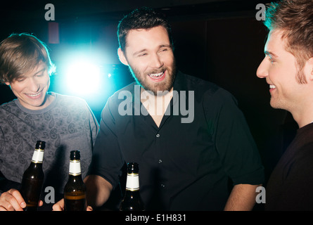 Three male friends drinking bottled beer in nightclub Stock Photo