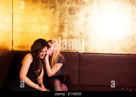 Two female friends whispering in nightclub Stock Photo
