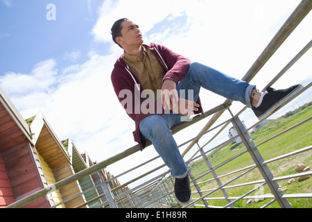 Portrait of young man sitting on beach hut fence Stock Photo