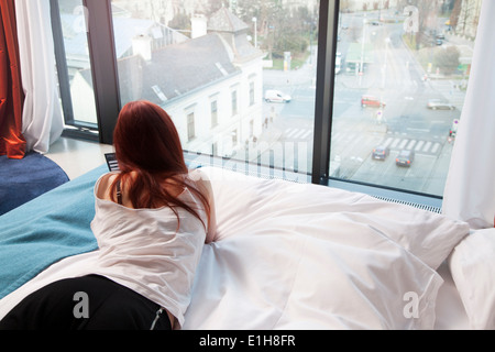 Young woman in hotel room overlooking street Stock Photo