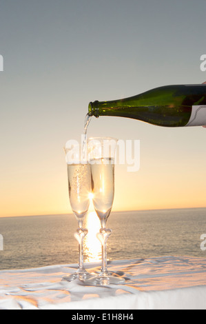 Champagne being poured into flute against sunset Stock Photo