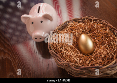 Golden Egg in Nest and Piggy Bank with American Flag Reflection on Wooden Table. Stock Photo