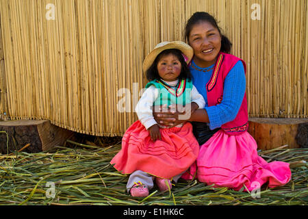 Friendly woman and a girl of the Uro Indians wearing traditional dress sitting in front of a reed hut, floating islands made of Stock Photo