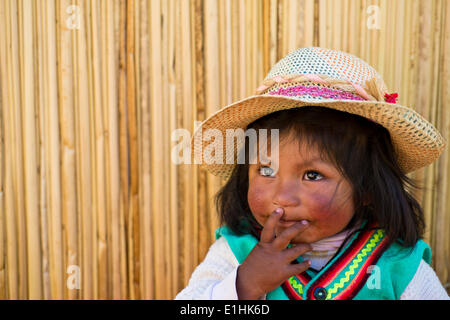 Young girl of the Uro Indians, about 6 years old, wearing traditional dress in front of a reed hut, floating islands made of Stock Photo
