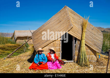 Two women of the Uro Indians wearing traditional dress sitting in front of a reed hut, floating islands made of totora reeds Stock Photo