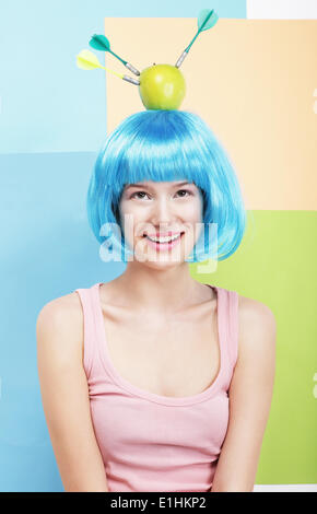 Precision. Amusing Woman in Blue Wig, Green Apple and Darts Stock Photo