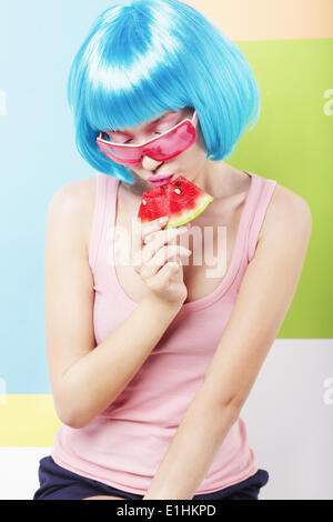 Trendy Woman in Blue Wig and ping Glasses Eating Watermelon