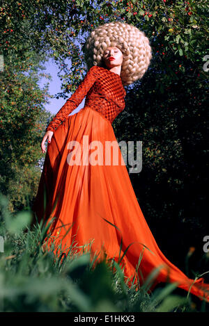 Fantasy. Artistic Stylized Woman in Trendy Red Dress and Big Frizzy Wig Stock Photo